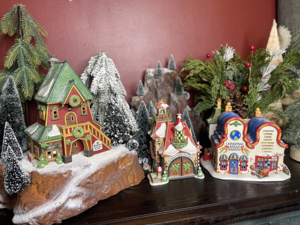 Shows step 3 of setting up a small Christmas village display: adding trees and evergreens