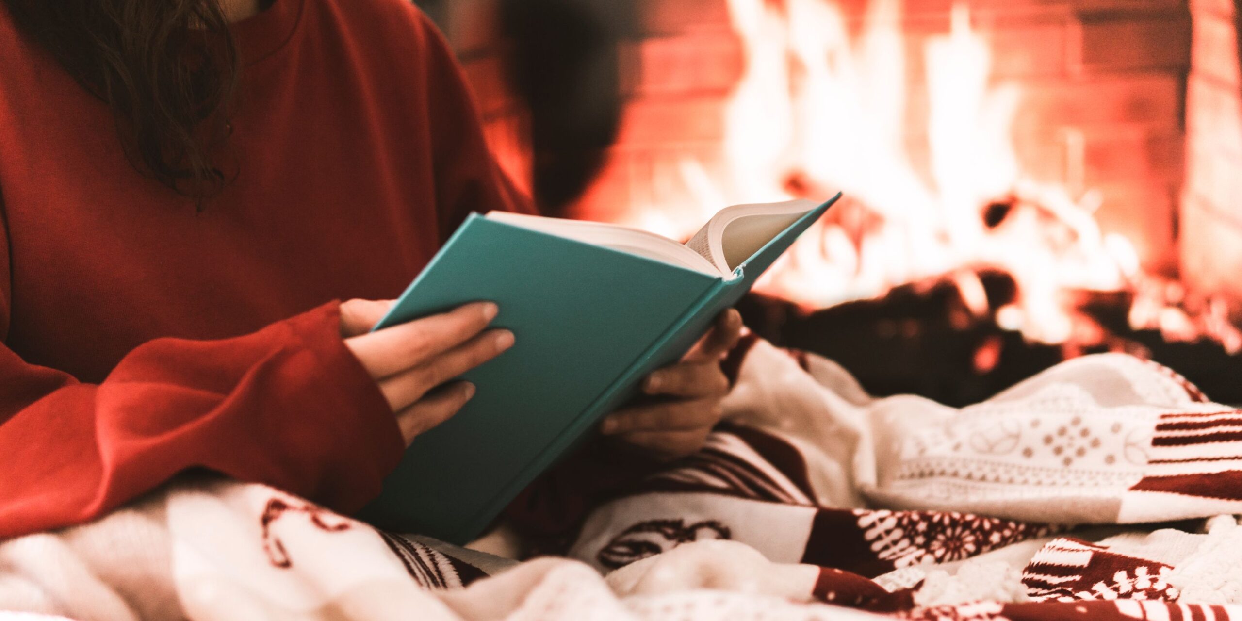 someone reading a Christmas romance book by a cozy fire